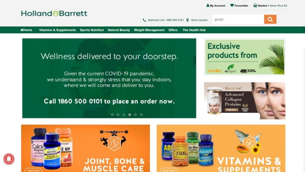 The Holland & Barrett India homepage: the wordmark and utility bar above a green navigation strip reading Vitamins & Supplements, Sports Nutrition, Natural Beauty, Weight Management, Offers and The Health Hub, with a wellness delivery banner and category promotions below.